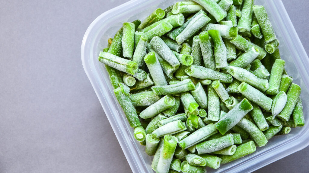 Frozen green beans in a plastic container for long-term storage. Deep freezing of vegetables. Frozen food vegetables on grey background. Stocking up vegetables for winter storage