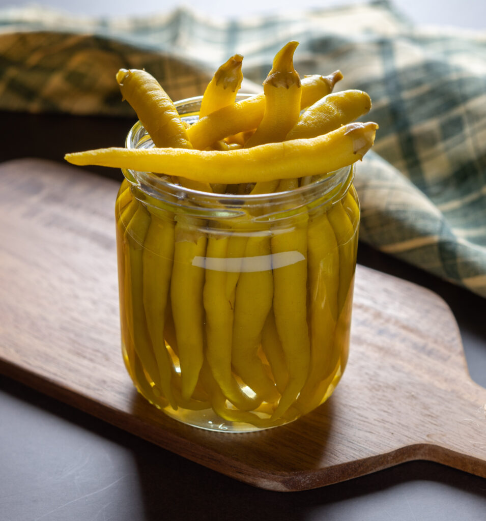 Front view of a jar of green peppers in vinegar.
